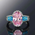 Platinum pink tourmaline ring - oval cut pink gemstone with diamond halo and blue side stones on white background